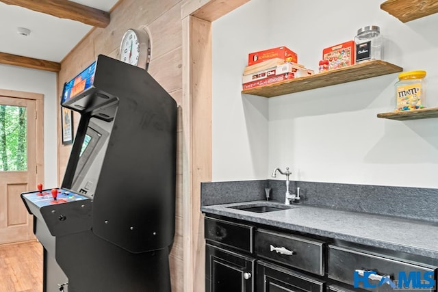 kitchen featuring a sink, dark cabinetry, light wood-type flooring, beam ceiling, and open shelves