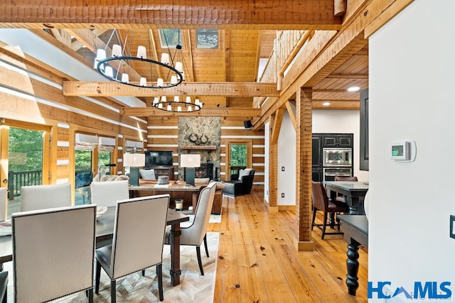 dining room featuring a stone fireplace, a high ceiling, wood walls, light wood-style floors, and a chandelier