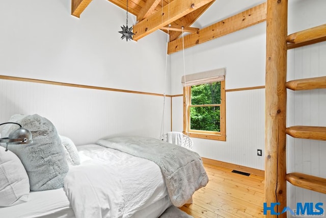 bedroom featuring a wainscoted wall, visible vents, vaulted ceiling with beams, and hardwood / wood-style flooring