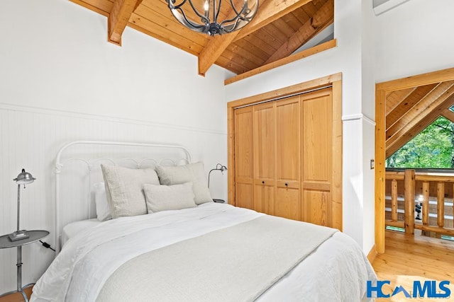 bedroom with lofted ceiling with beams, a chandelier, wooden ceiling, wood finished floors, and a closet