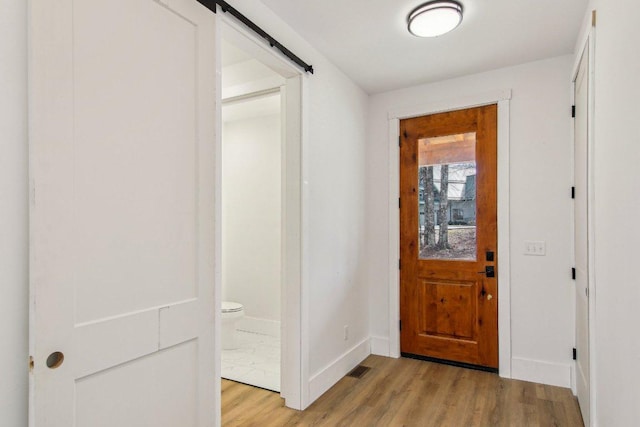 foyer entrance with baseboards, visible vents, light wood finished floors, and a barn door