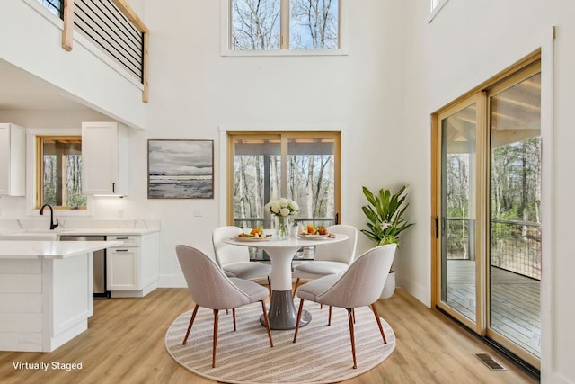 dining area featuring a towering ceiling, light wood-style flooring, visible vents, and baseboards