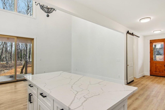 kitchen with a barn door, baseboards, white cabinets, light stone countertops, and light wood-type flooring