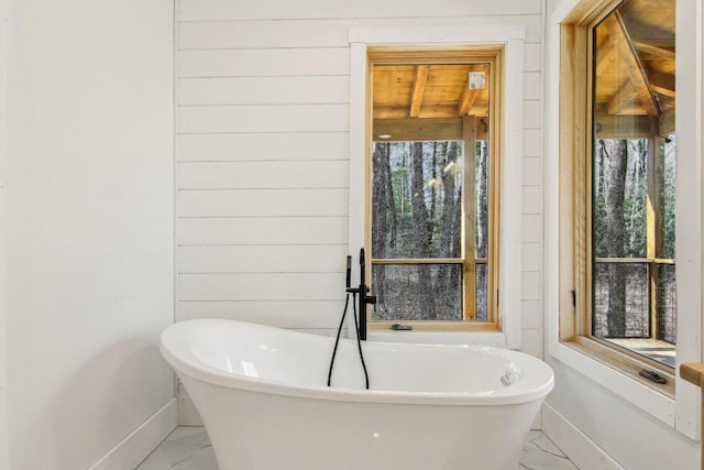 full bathroom featuring marble finish floor, baseboards, and a freestanding tub