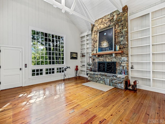 unfurnished living room with wood-type flooring, beamed ceiling, a stone fireplace, and built in shelves