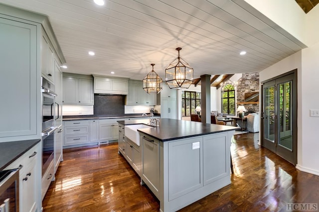 kitchen with dark hardwood / wood-style floors, pendant lighting, tasteful backsplash, an island with sink, and sink