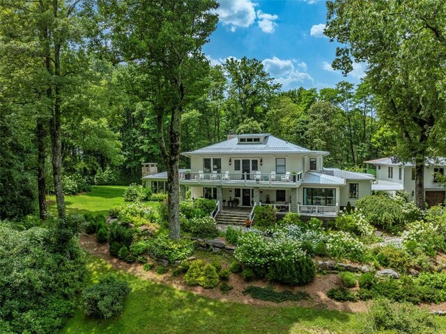 back of house featuring covered porch, a wooded view, metal roof, and a balcony