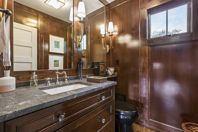 bathroom with toilet, vanity, wooden walls, and wood finished floors