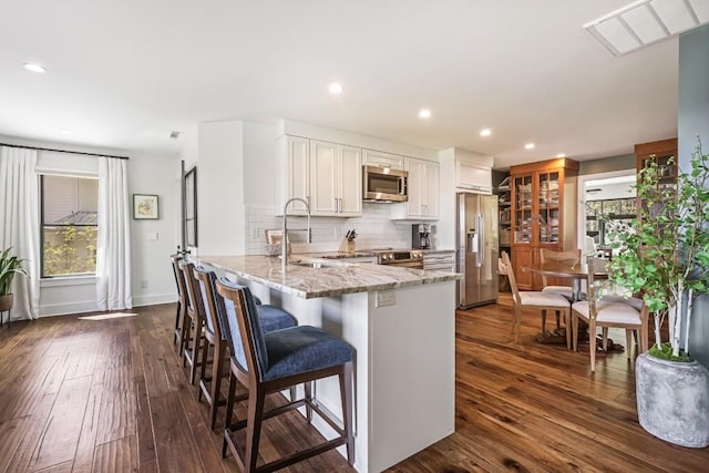 kitchen with appliances with stainless steel finishes, a sink, a peninsula, white cabinetry, and light stone counters