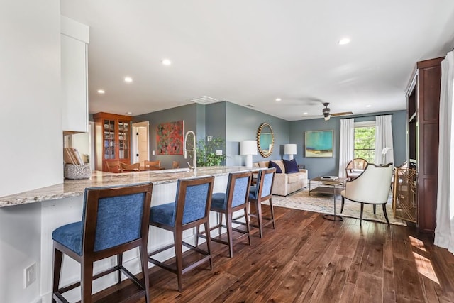 kitchen featuring dark wood-style floors, ceiling fan, a peninsula, a breakfast bar area, and light stone countertops