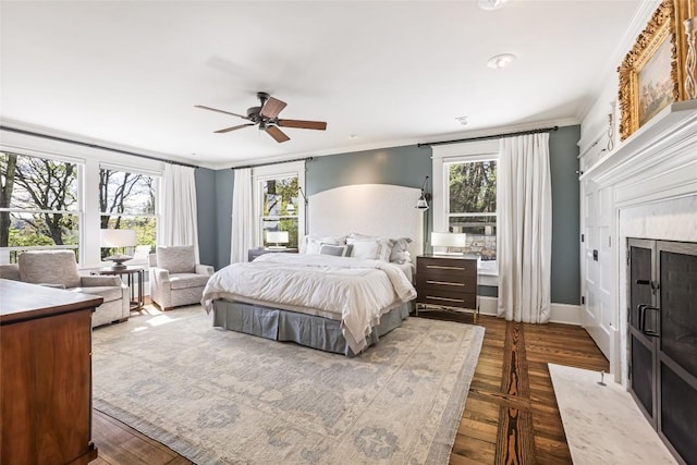 bedroom featuring multiple windows, crown molding, dark wood-type flooring, a fireplace, and ceiling fan