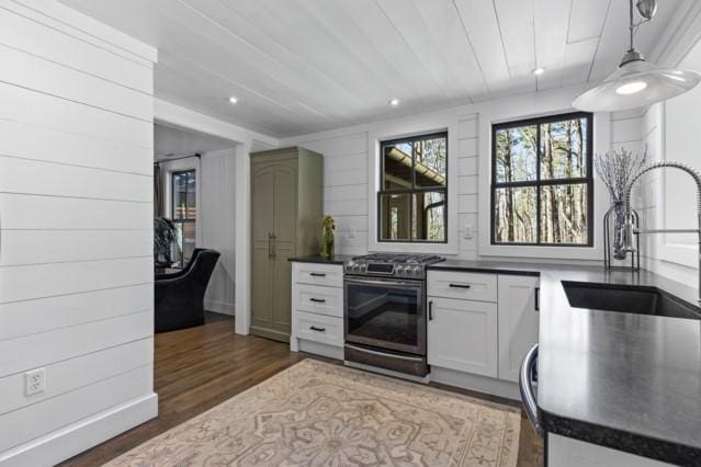 kitchen with a sink, light wood-type flooring, stainless steel gas range oven, and dark countertops