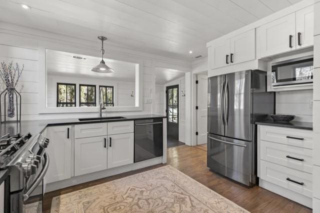 kitchen with white cabinets, a sink, dark wood finished floors, stainless steel appliances, and pendant lighting