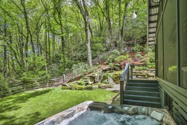 view of yard with an outdoor hot tub, a view of trees, and fence