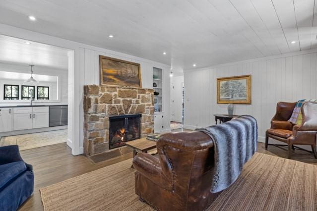 living room with wood finished floors, a stone fireplace, and recessed lighting