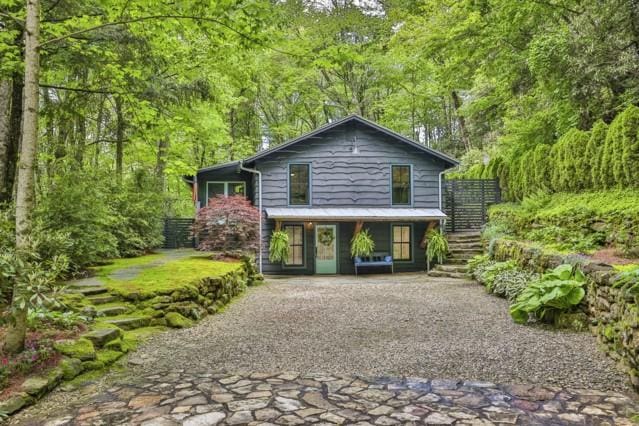 view of front of home featuring a view of trees, stairway, and gravel driveway