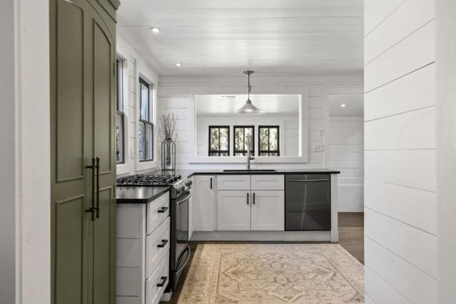 kitchen featuring black dishwasher, a sink, dark countertops, range with gas stovetop, and decorative light fixtures