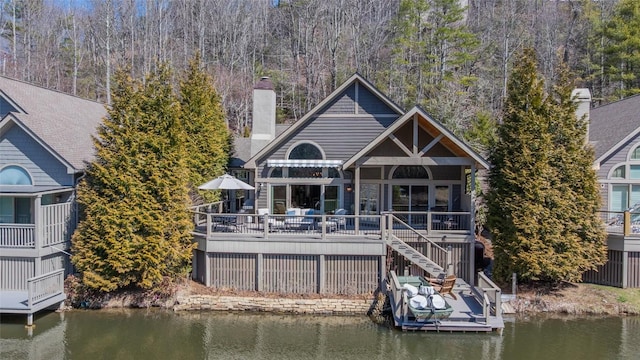 back of house featuring stairs, a deck with water view, a forest view, and a chimney