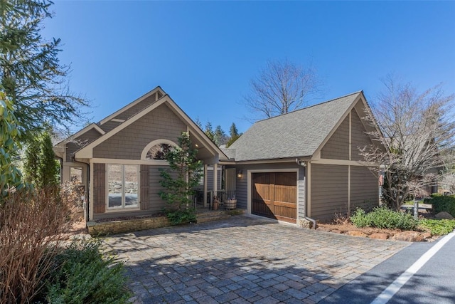 craftsman inspired home featuring decorative driveway, roof with shingles, and an attached garage