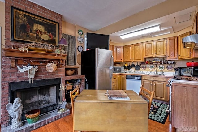 kitchen featuring light hardwood / wood-style flooring, sink, stainless steel appliances, ventilation hood, and a fireplace