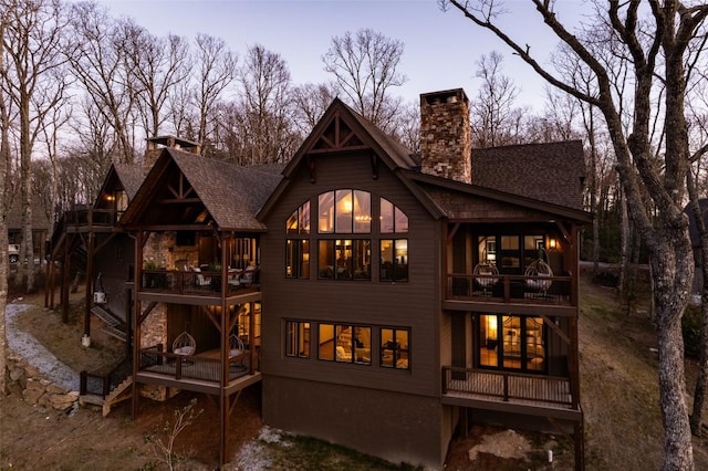 back of house with roof with shingles, a wooden deck, a chimney, and a balcony