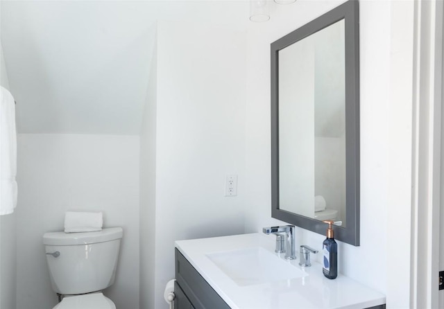 half bathroom with vanity, toilet, and lofted ceiling