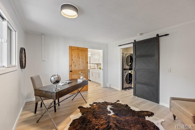 office area with stacked washing maching and dryer, a barn door, and light wood-type flooring