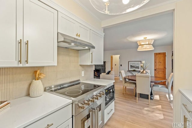 kitchen with a stone fireplace, tasteful backsplash, white cabinetry, cooktop, and light wood-type flooring