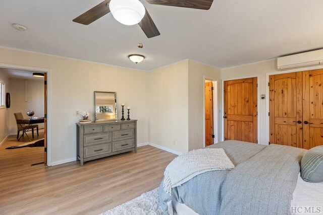 bedroom with a wall unit AC, ceiling fan, and light wood-type flooring