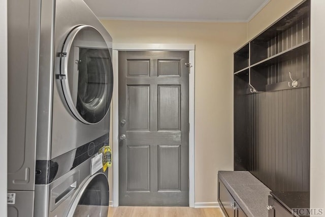 laundry area featuring stacked washer and dryer, ornamental molding, cabinets, and light wood-type flooring