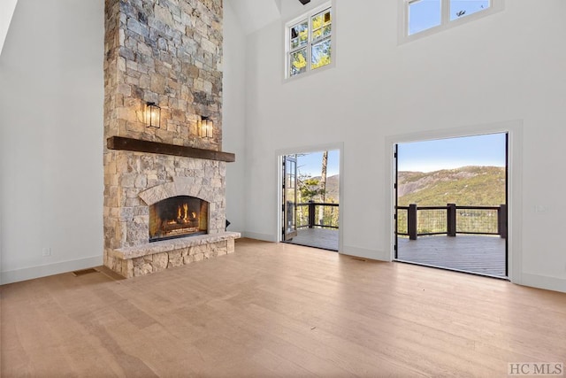 unfurnished living room featuring a mountain view, a towering ceiling, a stone fireplace, and light hardwood / wood-style floors