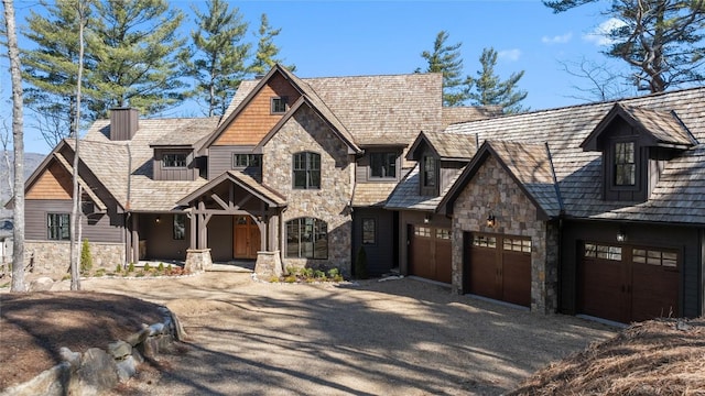 view of front of house with stone siding, an attached garage, a chimney, and gravel driveway