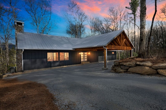 chalet / cabin featuring gravel driveway, a chimney, and metal roof