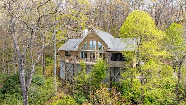 back of house with a view of trees, roof with shingles, and a wooden deck