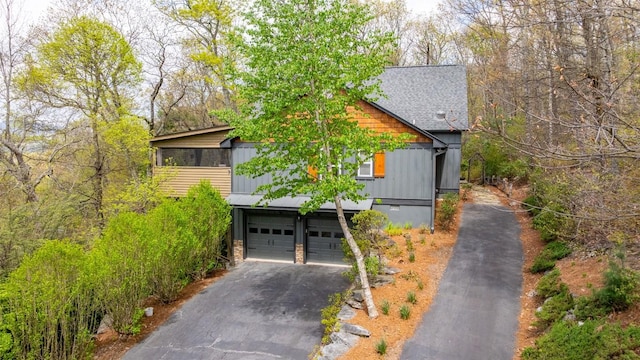 view of front of home with a shingled roof, an attached garage, driveway, and stone siding