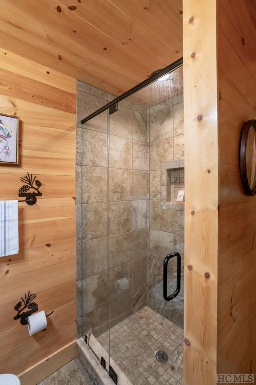 bathroom featuring toilet, wood walls, a shower with shower door, and wooden ceiling