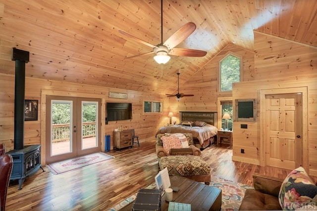 bedroom with french doors, high vaulted ceiling, access to exterior, wood walls, and a wood stove