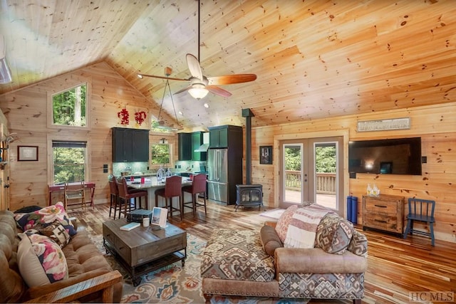 living room featuring light wood-type flooring, a wood stove, high vaulted ceiling, and wooden walls