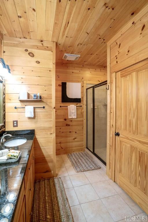 bathroom featuring vanity, wood walls, an enclosed shower, wooden ceiling, and tile patterned flooring