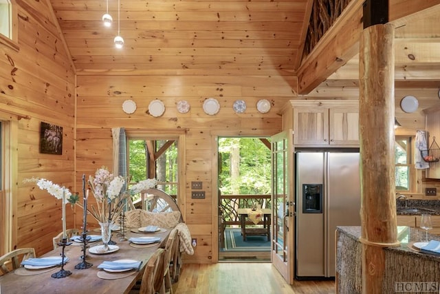 dining space with light wood-type flooring, sink, wooden ceiling, high vaulted ceiling, and wooden walls