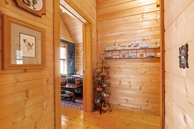 corridor with vaulted ceiling, wood walls, and hardwood / wood-style floors