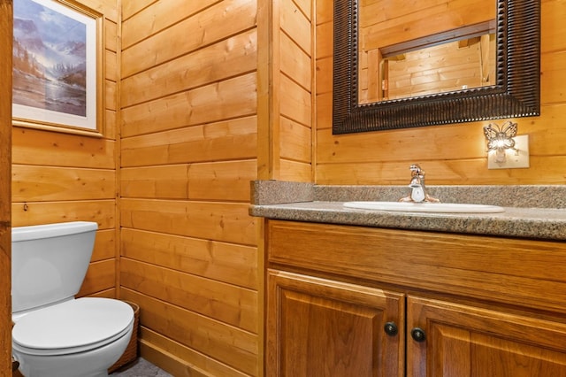 bathroom featuring toilet, vanity, and wood walls