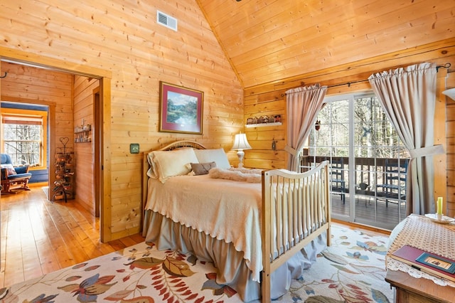 bedroom with wood walls, high vaulted ceiling, light wood-type flooring, and access to exterior