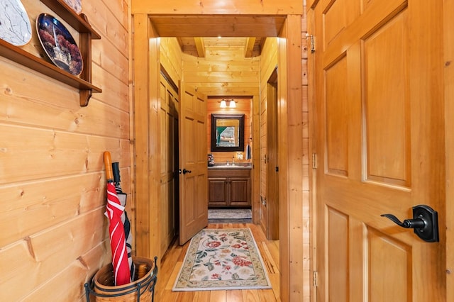 hallway with light hardwood / wood-style flooring, beamed ceiling, wood walls, and sink