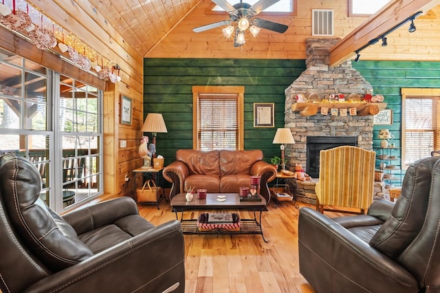 living room featuring hardwood / wood-style floors, vaulted ceiling, a fireplace, track lighting, and wooden walls