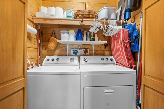 clothes washing area featuring wood walls and washer and clothes dryer