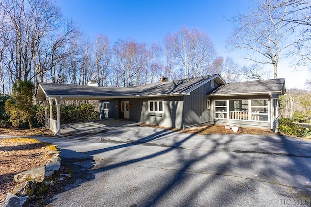 view of front facade featuring asphalt driveway, a chimney, a carport, and a porch