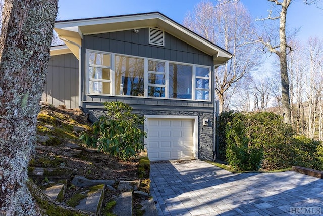 view of front of home with decorative driveway, stone siding, and an attached garage