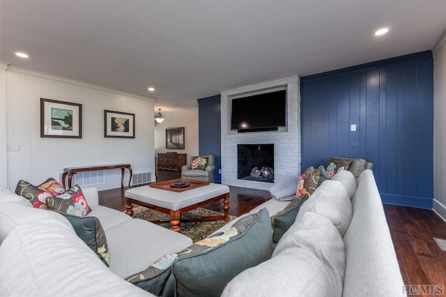 living room featuring ornamental molding, dark wood-type flooring, and a brick fireplace