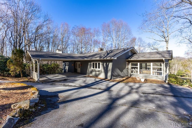 view of front facade with asphalt driveway, a chimney, and an attached carport